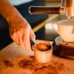 Dłoń baristy przygotowuje espresso w kolbowym ekspresie do kawy