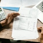 Ręce analizujące dokumenty finansowe przy laptopie i kalkulatorze