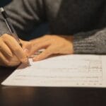 Mężczyzna w szarym swetrze wypełnia ważny formularz przy biurku
